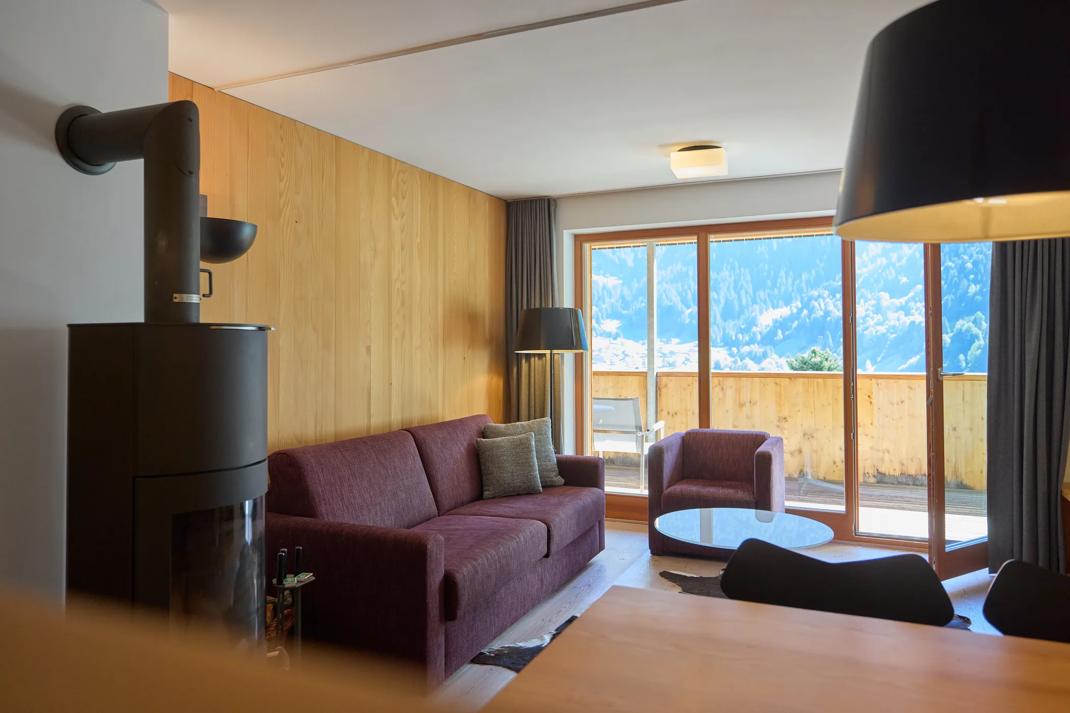Montafon Chalet 48 — Wohnbereich mit Kaminofen und Balkon mit Bergblick